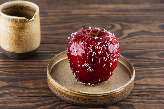 Baked apple with walnuts and honey in red glaze with coconut flakes on a wooden table.