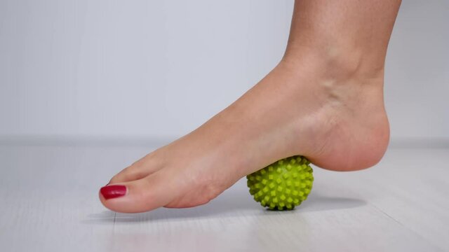 foot step on massage ball to relieve Plantar fasciitis or heel pain. woman with red pedicure massaging trigger points on her foot