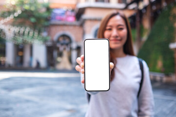 Mockup image of a young asian woman holding and showing a mobile phone with blank white screen while traveling in the city