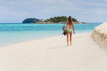 Fototapeta na wymiar Woman In bikini with beach bag walking on the beach in tropical island.
