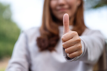 Closeup of a young woman making and showing thumbs up hand sign - obrazy, fototapety, plakaty