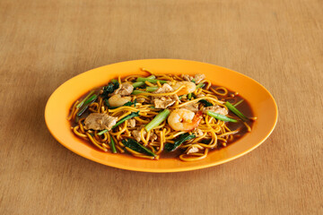 Delicious Singapore style Hokkien Mee noodles shrimps in orange plate on wooden background top view