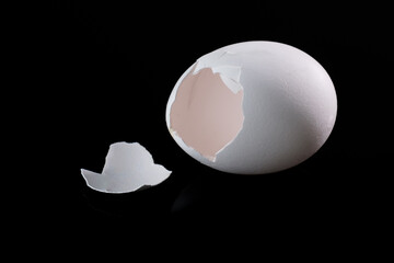 Aufgebrochenes, geknacktes leeres Ei / weiße Eierschale auf einem schwarzen neutralen Hintergrund freigestellt