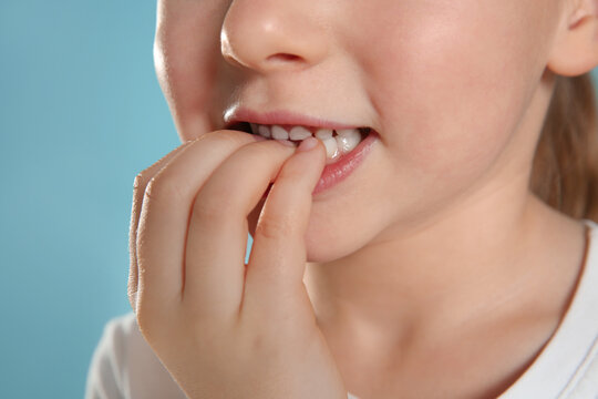 Little girl biting her nails on turquoise background, closeup
