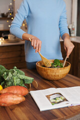 woman in blue shirt mixing salad  with green vegetables in the kitchen