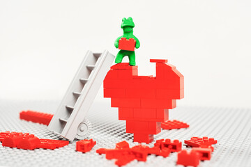 Concept. Build your own happiness. A green plasticine man builds a huge heart out of plastic blocks