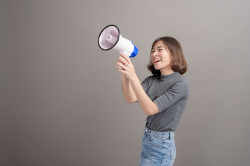 Portrait of young beautiful asian woman holding megaphone over studio background.