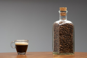 Glass cup of espresso and bottle of coffee beans.   - 480382378