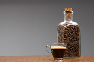 Glass cup of espresso and bottle of coffee beans.   - 480382380