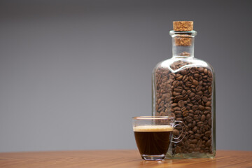Glass cup of espresso and bottle of coffee beans.   - 480382383