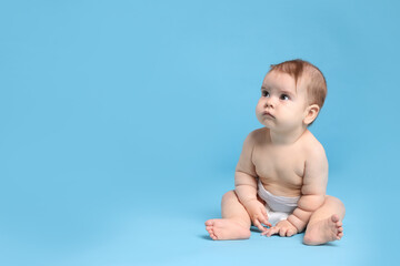 Cute little baby in diaper sitting on light blue background. Space for text