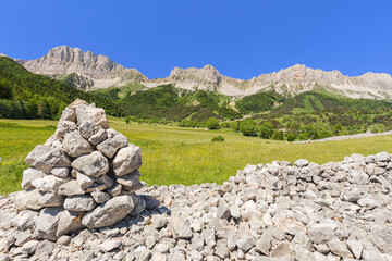 Fototapeta na wymiar Rocaille avec cairn, falaise et ligne de crête de plateaux calcaires. Balcon Est du Vercors, réserve naturelle des Hauts Plateaux, Grand Veymont.