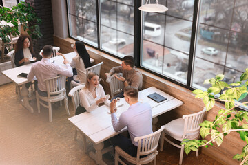 Coworkers having coffee break near window in cafe, above view
