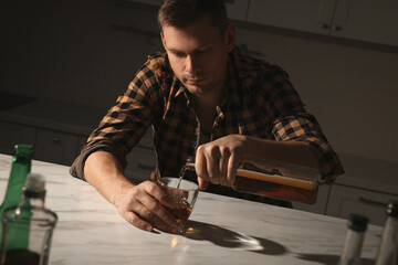 Addicted man with alcoholic drink at table in kitchen