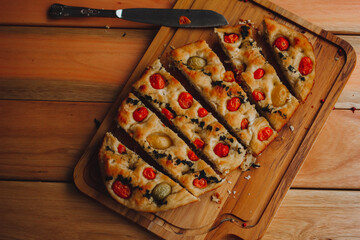 Homemade Italian Focaccia, with tomato and olive oil on a rustic wooden background.