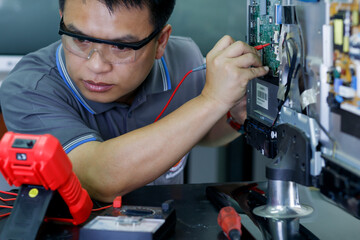 The technician is using a screwdriver to remove the TV board to repair the TV. The concept of a professional TV repair technician.