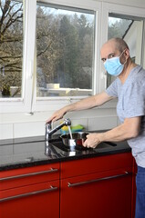 Hausmann mit Maske in der Küche