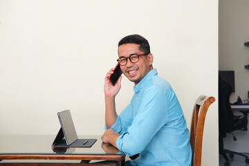 Adult Asian man smiling confident when sitting in front of his mobile tablet gadget
