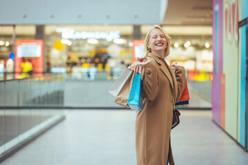 Woman enjoying the weekend in the shopping mall. Beautiful young woman with shopping bags looking at camera with smile while standing at the store.