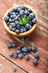 Blueberry berries with mint leaves are in a wooden plate on wooden background.