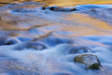 Spring landscape of the Little River captured with motion blur and illuminated by reflected color from sunlit foliage and blue sky overhead, Great Smoky Mountains National Park, Tennessee, USA