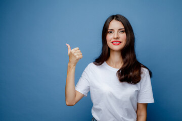Brunette woman with long hair in a white T-shirt points her thumb to the side