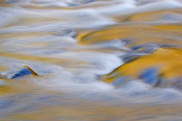Spring landscape of the Little River captured with motion blur and illuminated by reflected color from sunlit foliage and blue sky overhead, Great Smoky Mountains National Park, Tennessee, USA
