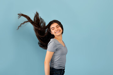 Portrait of smiling Indian teenage girl posing with long dark flying hair on blue studio background