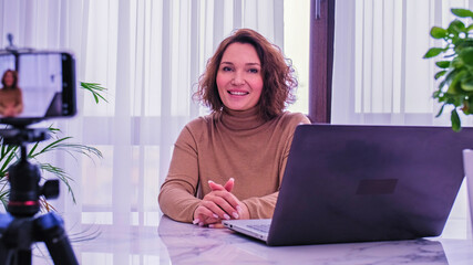 Smiling woman recording her video blog. Woman blogger videotapes her vlog at home.  Adult woman...