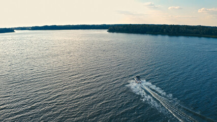 Photo from a drone above a river with a fast driving speedboat while sunset. Aerial view of driving powerboat on lake.. - obrazy, fototapety, plakaty