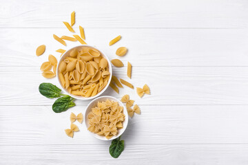 Fototapeta na wymiar Mix of Italian raw pasta in white bowls with spinach leaves