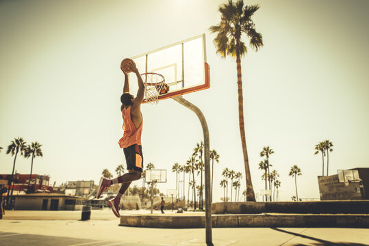 Young players playing basketball at the court in venice beach, California. Professional street ballers having fun performing tricks and huge slam dunks