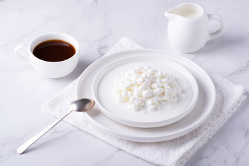 Fresh cottage cheese grain in a white bowl and coffee. Curd in granules with cream