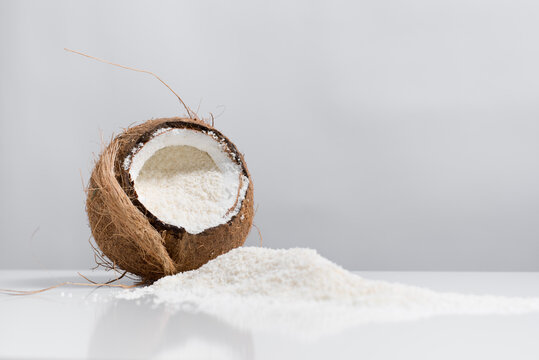 Coco abierto con hojuelas de coco ralladas derramadas sobre una mesa blanca	