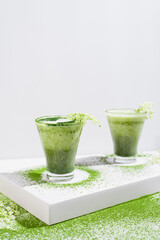 Dos vasos de té matcha con leche decorado con flores y polvo de té verde espolvoreado sobre una mesa blanca	