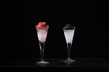 Caviar de esturión negro y caviar de salmón rojo servido en copa de cóctel helada sobre fondo negro	