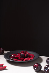 Rodajas de ciruelas negras y ciruelas enteras en un plato negro sobre una mesa gris