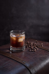 Vaso de café frío con hielo y granos de café en una vieja maleta marrón sobre fondo oscuro	
