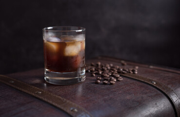 Vaso de café frío con hielo y granos de café en una vieja maleta marrón sobre fondo oscuro	