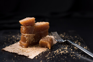 Dulce pasta de gelatina de membrillo dorado con s&eacute;samo molido y un tenedor sobre una placa de madera negra	