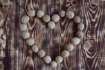 Flat lay top view of a rustic brown wooden table on which a heart shape symbol made from unpeeled walnuts is laid out, a sign expressing love and support, copy space.
