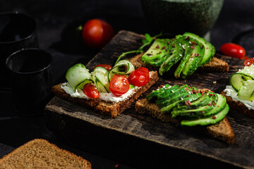 Toast with cream cheese, avocado, cucumber and tomato on a table