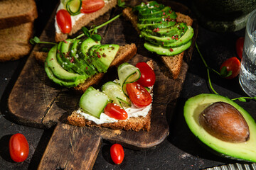 Toast with cream cheese, avocado, cucumber and tomato on a table