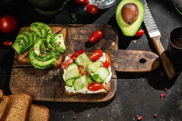 Toast with cream cheese, avocado, cucumber and tomato on a table