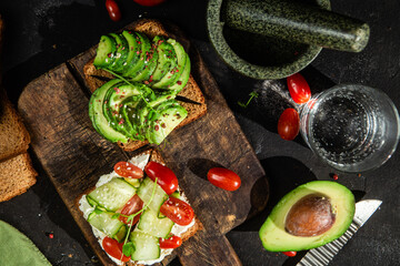 Toast with cream cheese, avocado, cucumber and tomato on a table