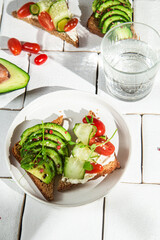 Toast with cream cheese, avocado, cucumber and tomato on a table
