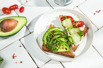 Toast with cream cheese, avocado, cucumber and tomato on a table