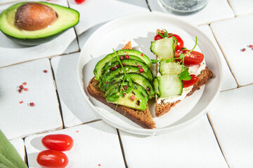 Toast with cream cheese, avocado, cucumber and tomato on a table