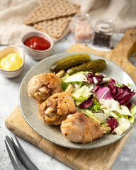 Fried chicken legs with salad and pickles in a plate on a light gray kitchen table. Cooked poultry meat in close-up on a culinary background	