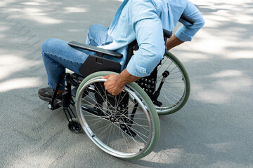 Unrecognizable young black disabled guy in wheelchair enjoying walk at park, closeup